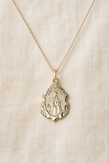 Gold Filled St Dymphna medal necklace with a religious pendant on a beige fabric background