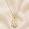 St Dymphna 14KT Gold Filled necklace with a pendant on a beige fabric background