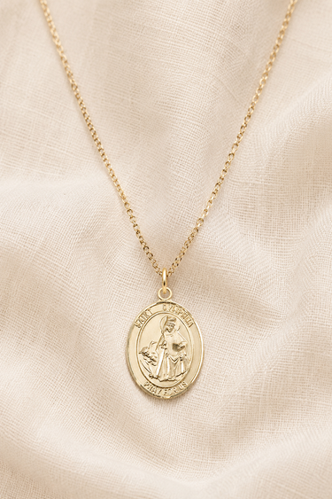 St Dymphna 14KT Gold Filled necklace with a pendant on a beige fabric background