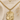 A gold Air Force pendant necklace displayed on a beige fabric background with decorative dried flowers. The image includes text reading 'AIR FORCE' and '14 KT GOLD FILLED' with a winged emblem above.