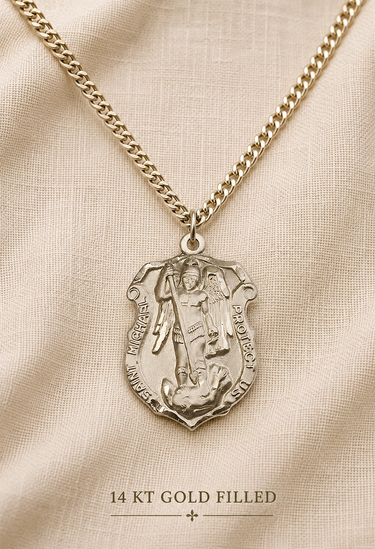 A gold-filled Saint Michael medal pendant necklace on a textured chain, displayed on a beige fabric background with the text '14 KT GOLD FILLED' at the bottom.
