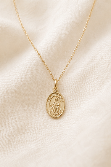 14KT Gold Filled St Dymphna medal necklace with a pendant on a beige fabric background