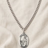 Sterling Silver St Dymphna necklace with a oval pendant on a beige fabric background and 24" chain