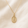 14KT Gold Filled St Dymphna medal necklace with a pendant on a beige fabric background
